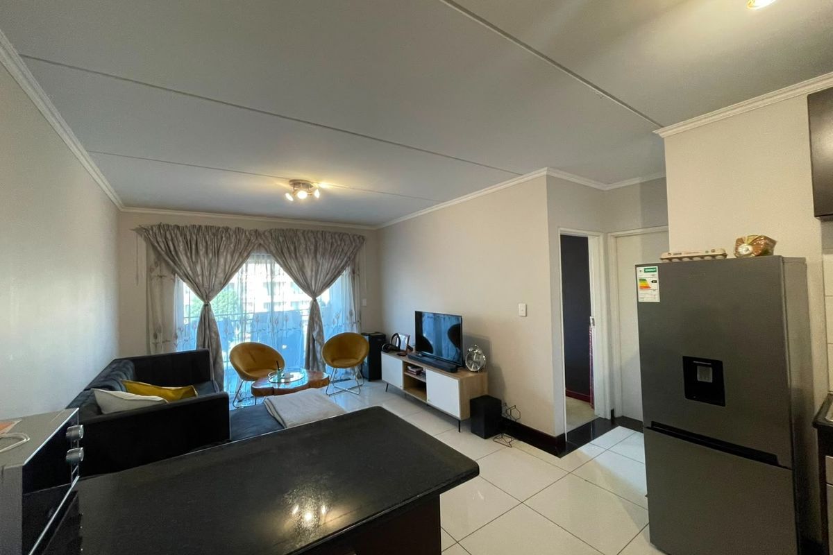Open plan living area featuring tiled flooring, a kitchen breakfast bar, and sliding door access to a balcony, creating a bright and functional space.