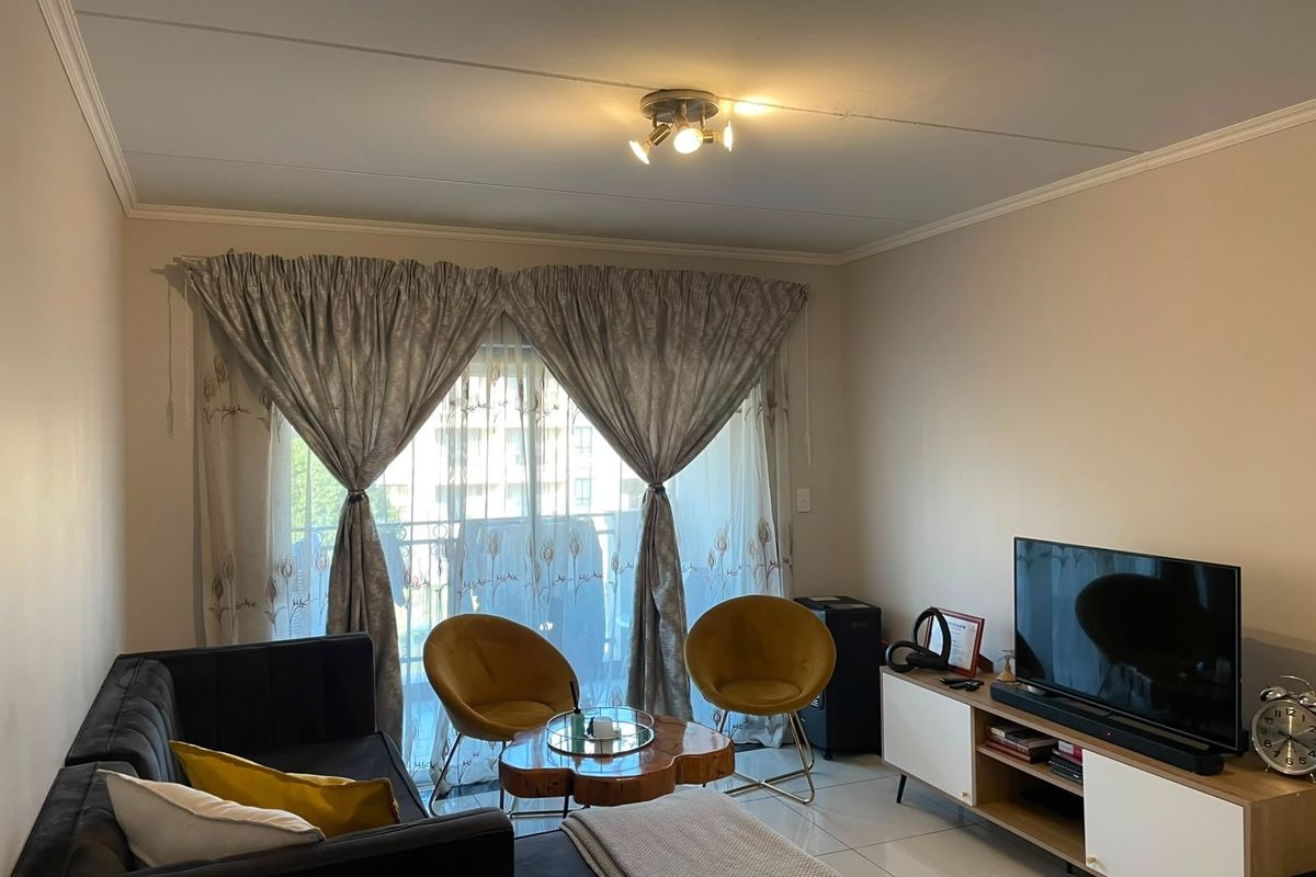 A well-maintained living room featuring tiled flooring, a modern ceiling spotlight fixture, and a sliding glass door providing access to the balcony.