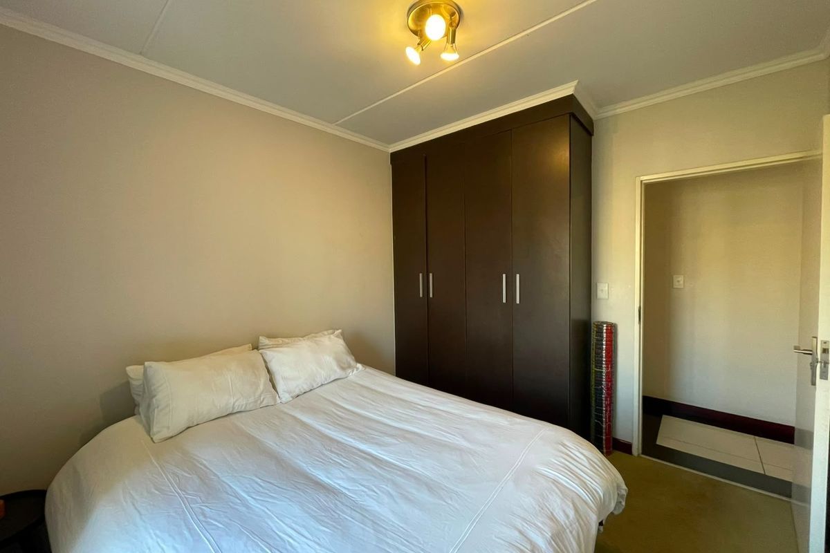 A bedroom featuring a dark wood built-in wardrobe, neutral wall finishes, and a ceiling light fixture.