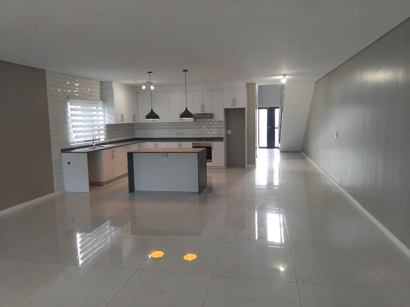 Spacious open-plan living area featuring a modern kitchen with white cabinetry, a central island, subway tile backsplash, and polished porcelain floor tiles throughout.