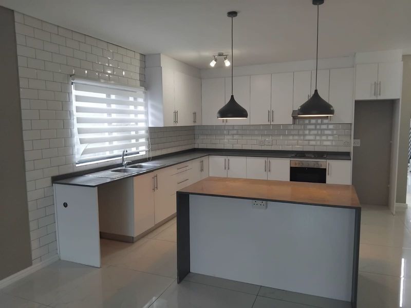 Modern kitchen featuring white cabinetry, subway tile backsplash, a central island, built-in oven, hob, and sleek pendant lighting.
