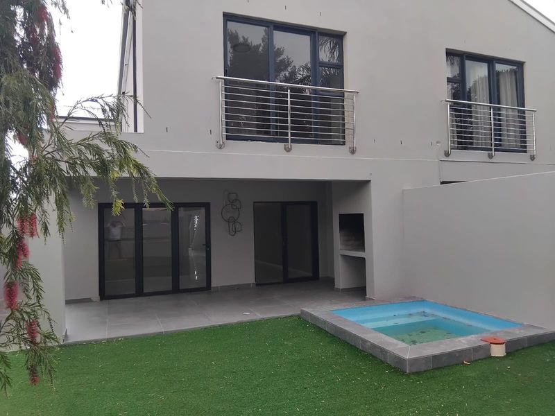 Rear exterior view featuring a covered patio with a built-in braai, a small plunge pool, and upper-level balconies with stainless steel railings.
