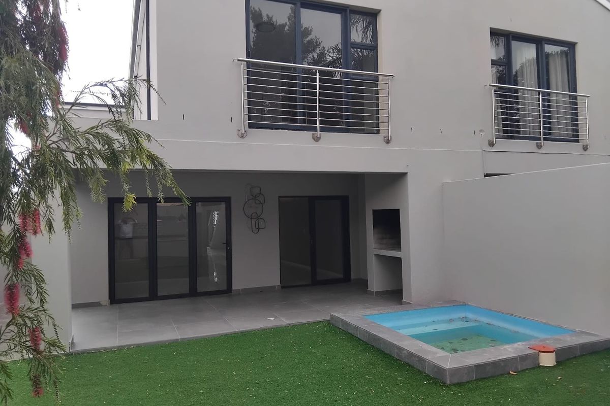 Rear exterior view featuring a covered patio with a built-in braai, a small plunge pool, and upper-level balconies with stainless steel railings.