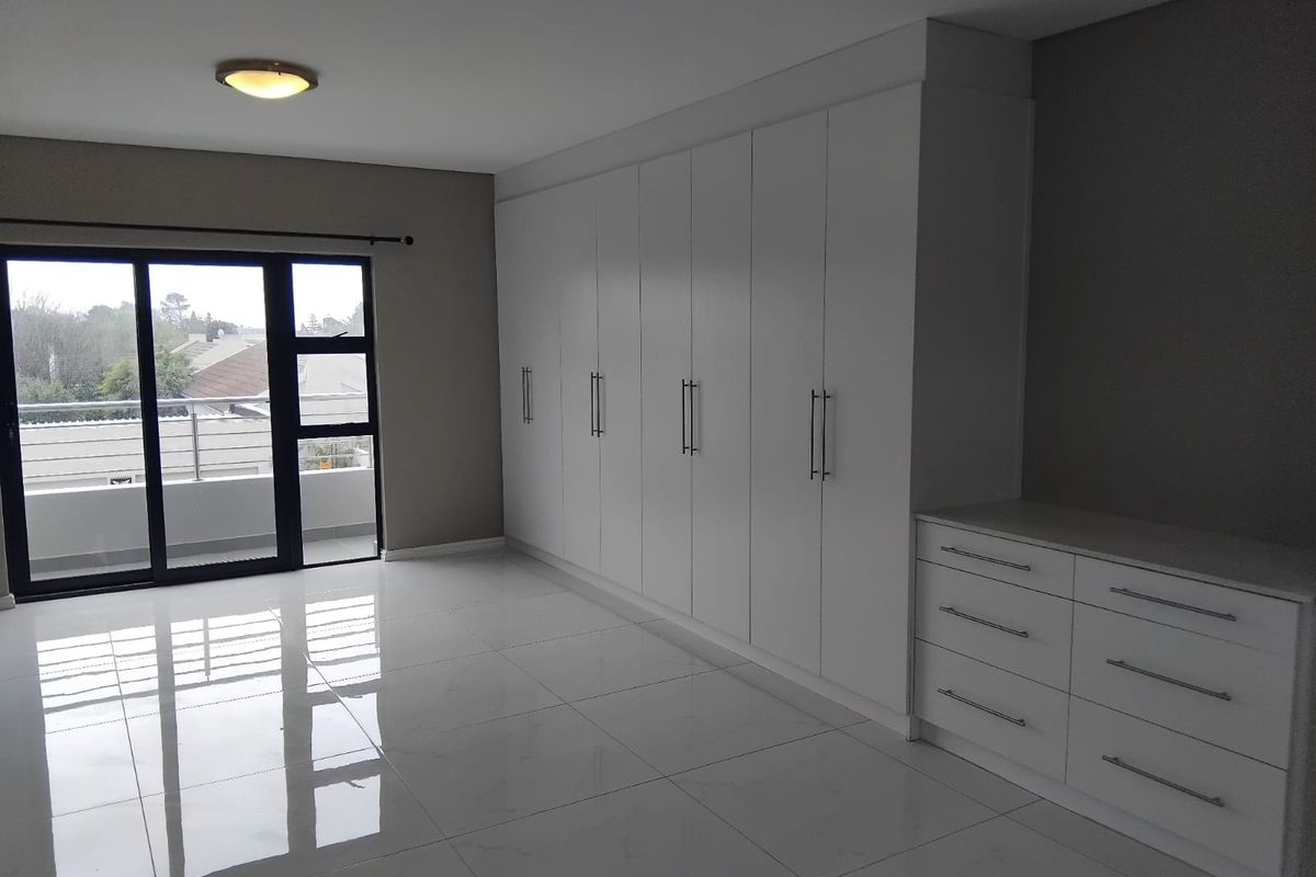 Spacious bedroom featuring extensive built-in cabinetry, a matching vanity unit, polished tiled floors, and a sliding door leading to a private balcony.