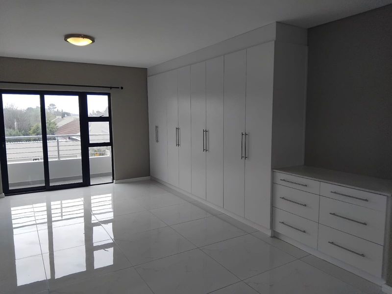 Spacious bedroom featuring extensive built-in cabinetry, a matching vanity unit, polished tiled floors, and a sliding door leading to a private balcony.