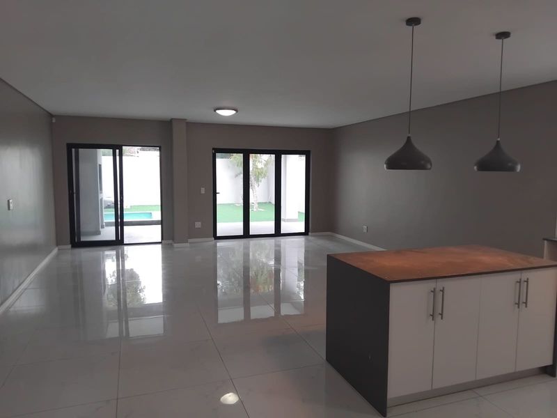 Spacious open-plan living area featuring a modern kitchen island, sleek porcelain flooring, and large sliding glass doors providing seamless access to the outdoor pool area.