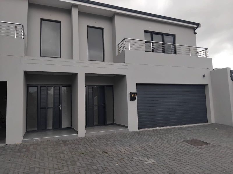 Modern double-storey townhouse facade featuring a paved driveway, double garage, and an upper-level balcony with stainless steel balustrades.