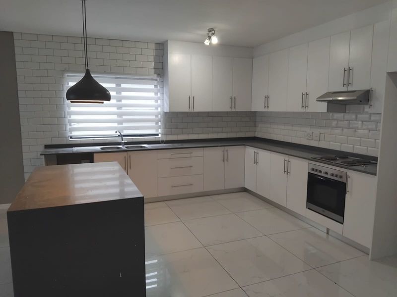 Modern kitchen featuring white cabinetry, quartz countertops, subway tile backsplash, built-in oven, hob, extractor fan, and large porcelain floor tiles.