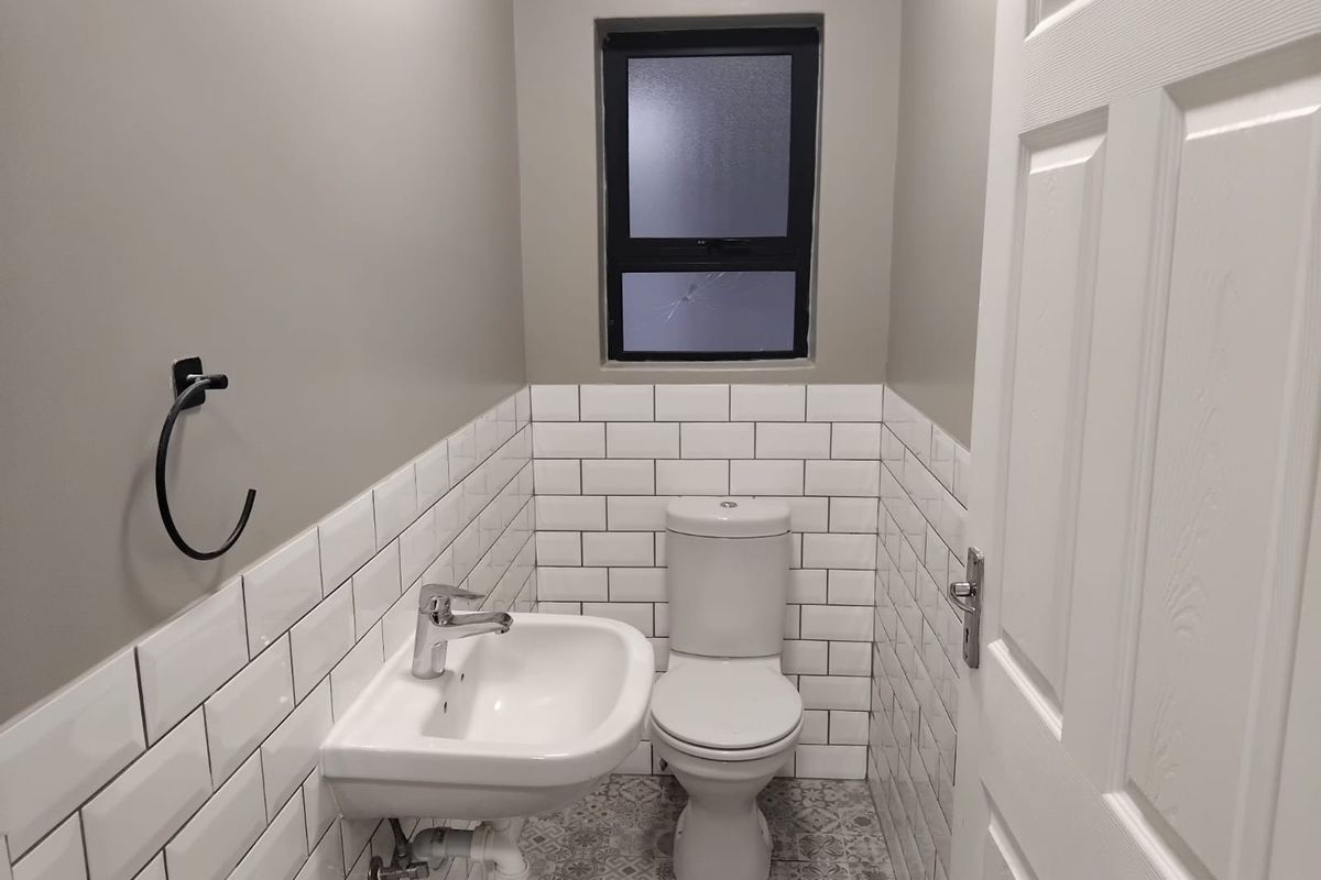 A compact, modern bathroom featuring white subway wall tiles, patterned floor tiles, a wall-mounted basin, and a toilet.