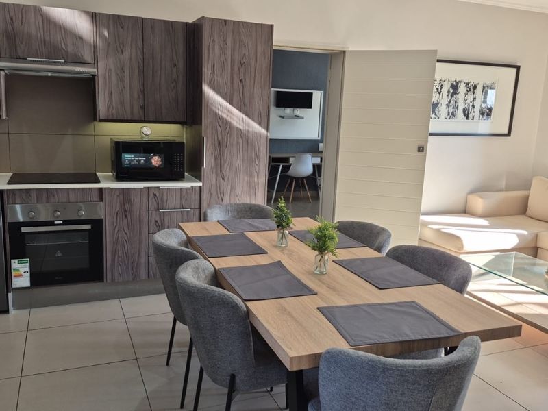 Modern open-plan living area featuring a contemporary kitchen with built-in appliances, tiled flooring, and seamless flow into the dining and lounge space.