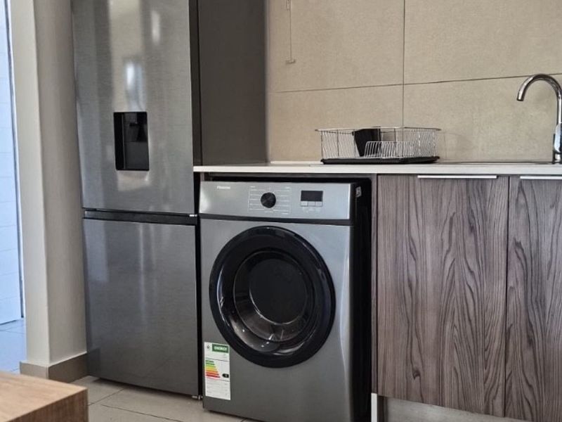A compact laundry area featuring built-in cabinetry, a stainless steel sink, tiled backsplash, and tiled flooring, providing a functional and modern utility space.