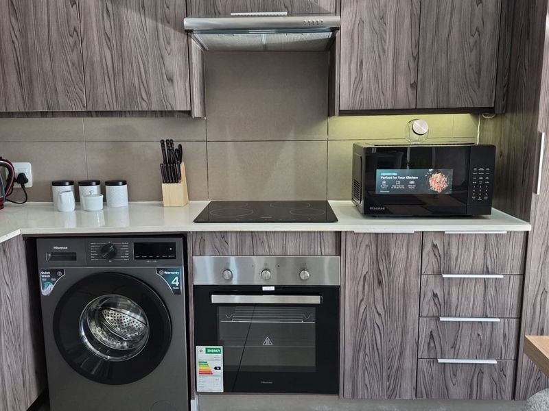 Modern kitchen featuring wood-grain cabinetry, stone countertops, integrated washing machine, and built-in stainless steel oven with electric hob.