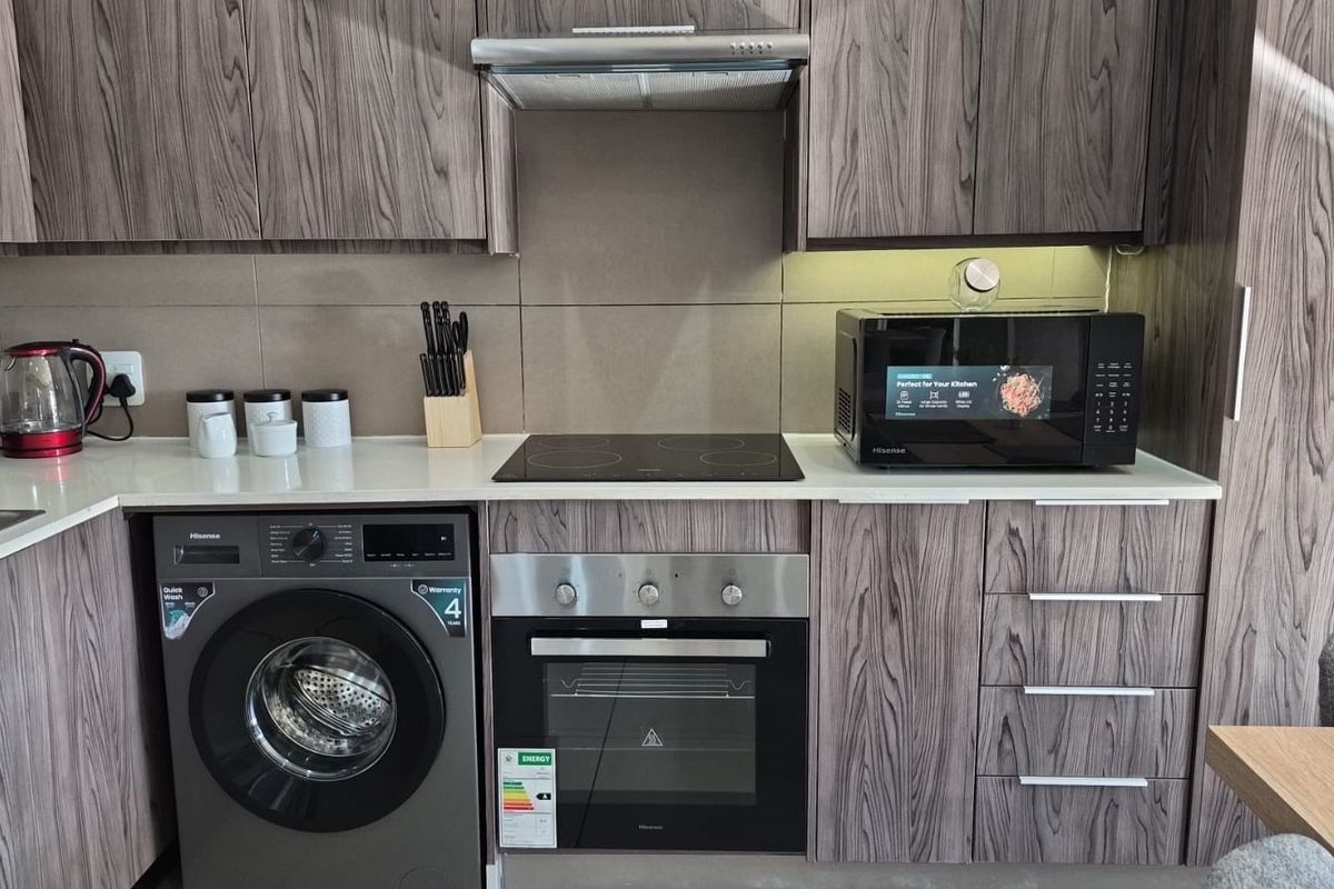 Modern kitchen featuring wood-grain cabinetry, stone countertops, integrated washing machine, and built-in stainless steel oven with electric hob.