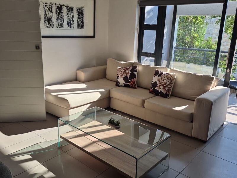 A bright living room featuring large sliding glass doors that open onto a balcony, with neutral tiled flooring throughout.