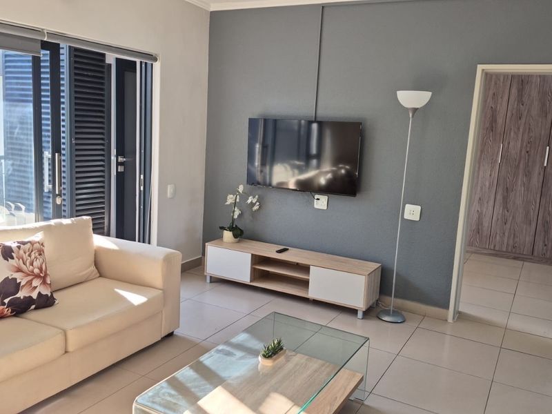 A bright living room featuring tiled flooring, a feature wall, and a sliding glass door providing access to an outdoor balcony area.