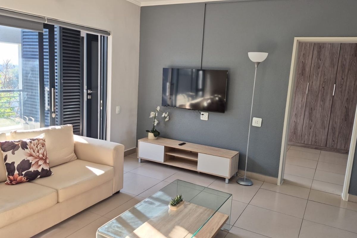 A bright living room featuring tiled flooring, a feature wall, and a sliding glass door providing access to an outdoor balcony area.