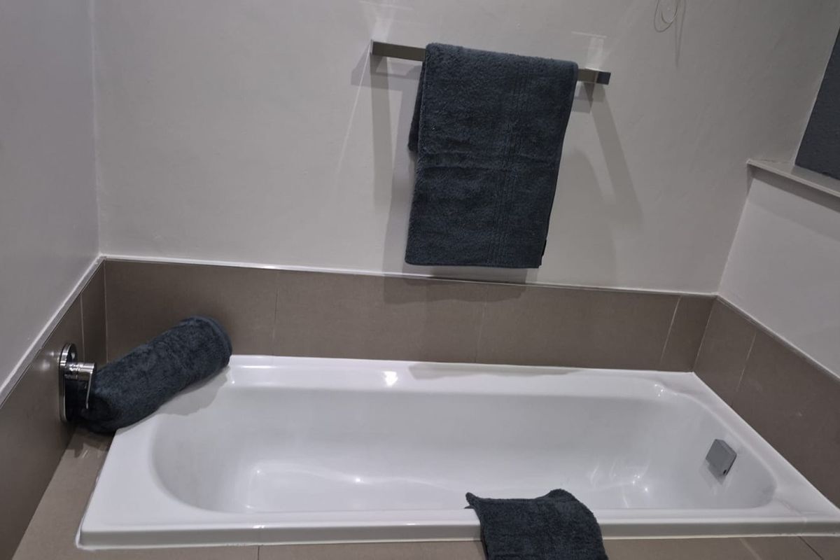 A clean bathroom featuring a built-in bathtub with neutral tiled surround and a wall-mounted towel rail.