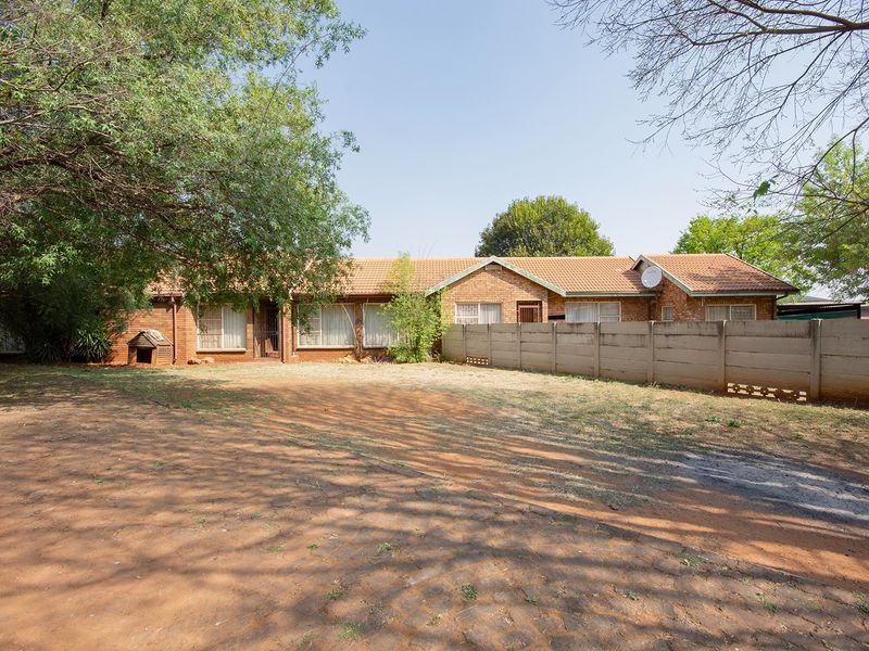 Rear view of a single-story brick house featuring a tiled roof and a large, open garden area enclosed by a precast concrete boundary wall.