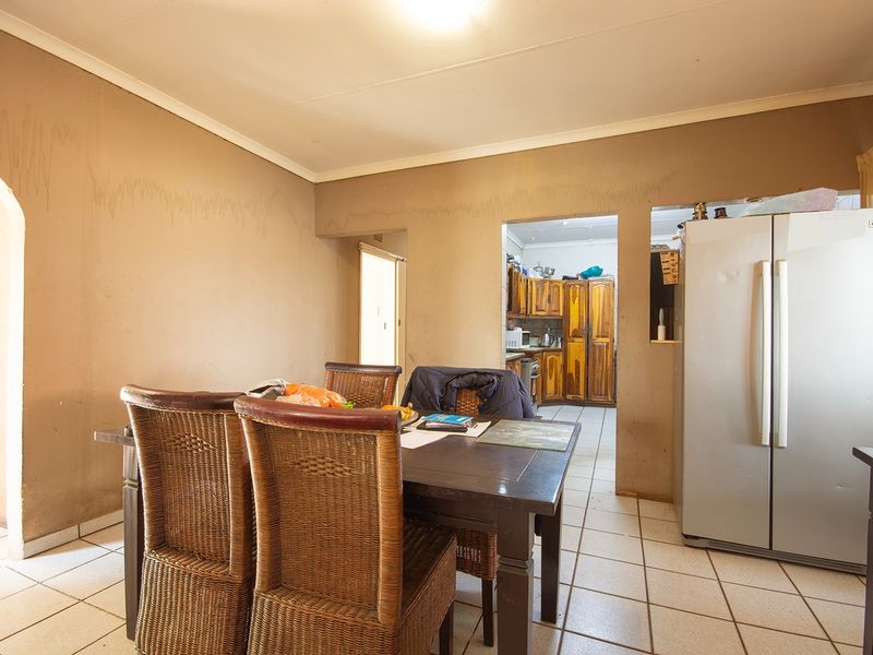 Open plan dining area with tiled flooring and an adjacent kitchen, showing signs of wear on the walls.