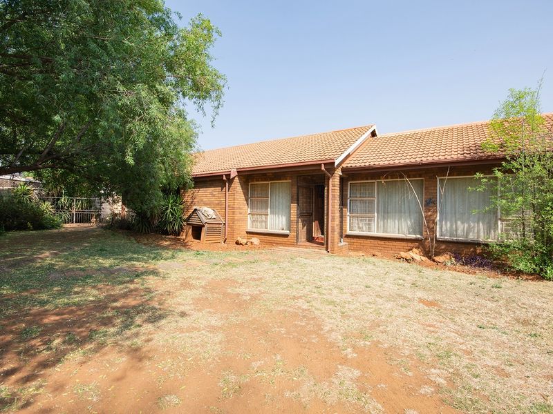 Rear view of a face brick house featuring a tiled roof and established garden area with mature trees.