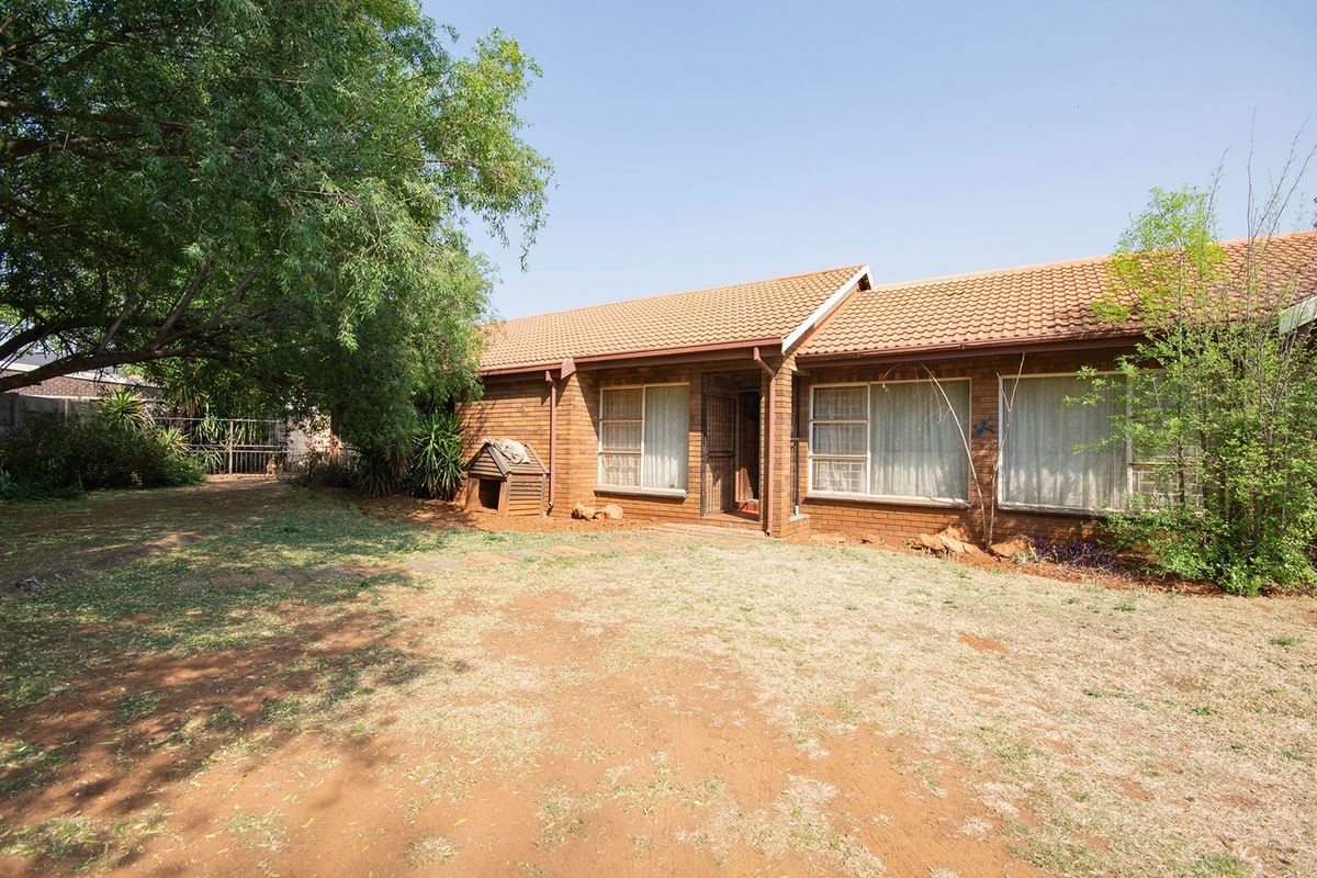 Rear view of a face brick house featuring a tiled roof and established garden area with mature trees.