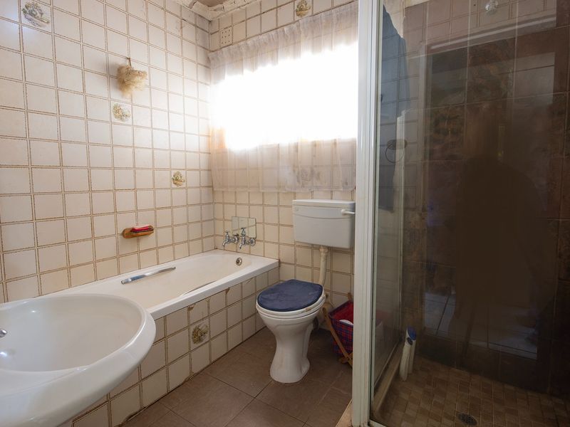A dated bathroom featuring a built-in bathtub, separate shower enclosure, pedestal basin, and toilet, requiring cosmetic updates to the ceiling and tiling.