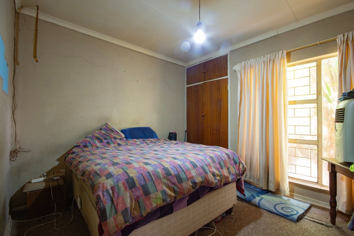 A bedroom featuring a built-in wardrobe, security bars on the window, and coving, requiring cosmetic updates to improve the overall finish.
