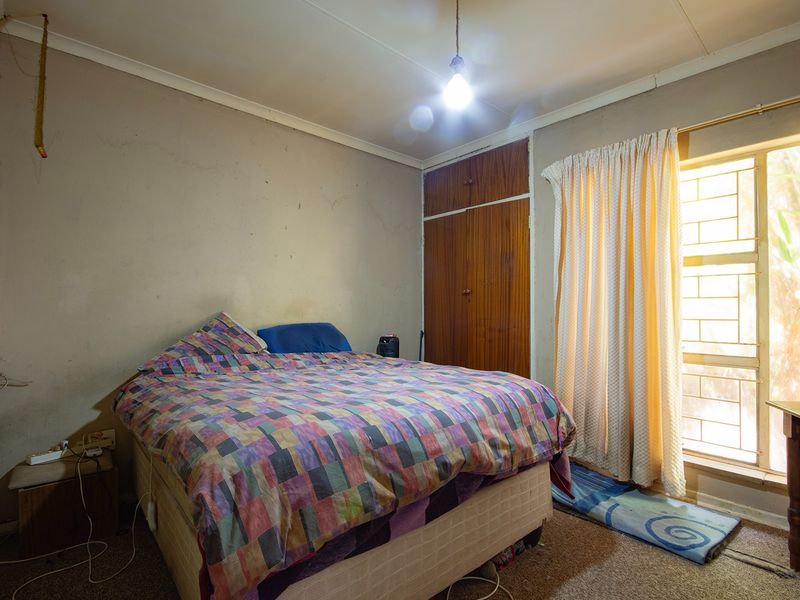 A bedroom featuring a built-in wardrobe, security bars on the window, and coving, requiring cosmetic updates to improve the overall finish.