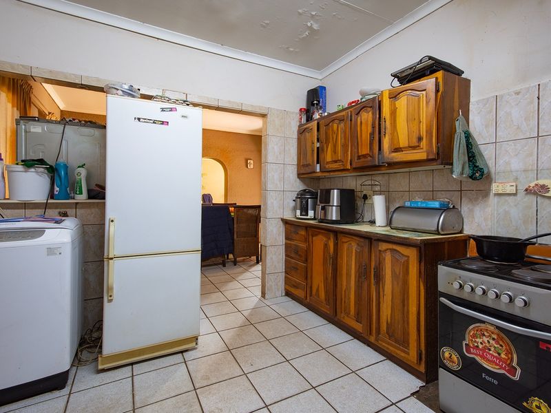 A functional kitchen featuring wooden cabinetry, tiled flooring, and a tiled backsplash, requiring some ceiling maintenance and cosmetic updates.