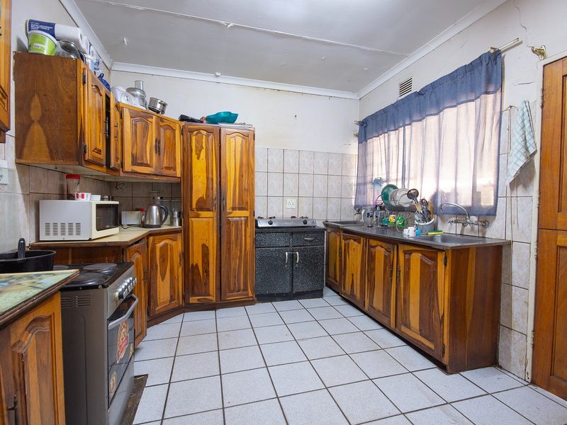 A dated kitchen featuring wooden cabinetry, tiled flooring, and a tiled backsplash, offering significant potential for modernization and renovation.