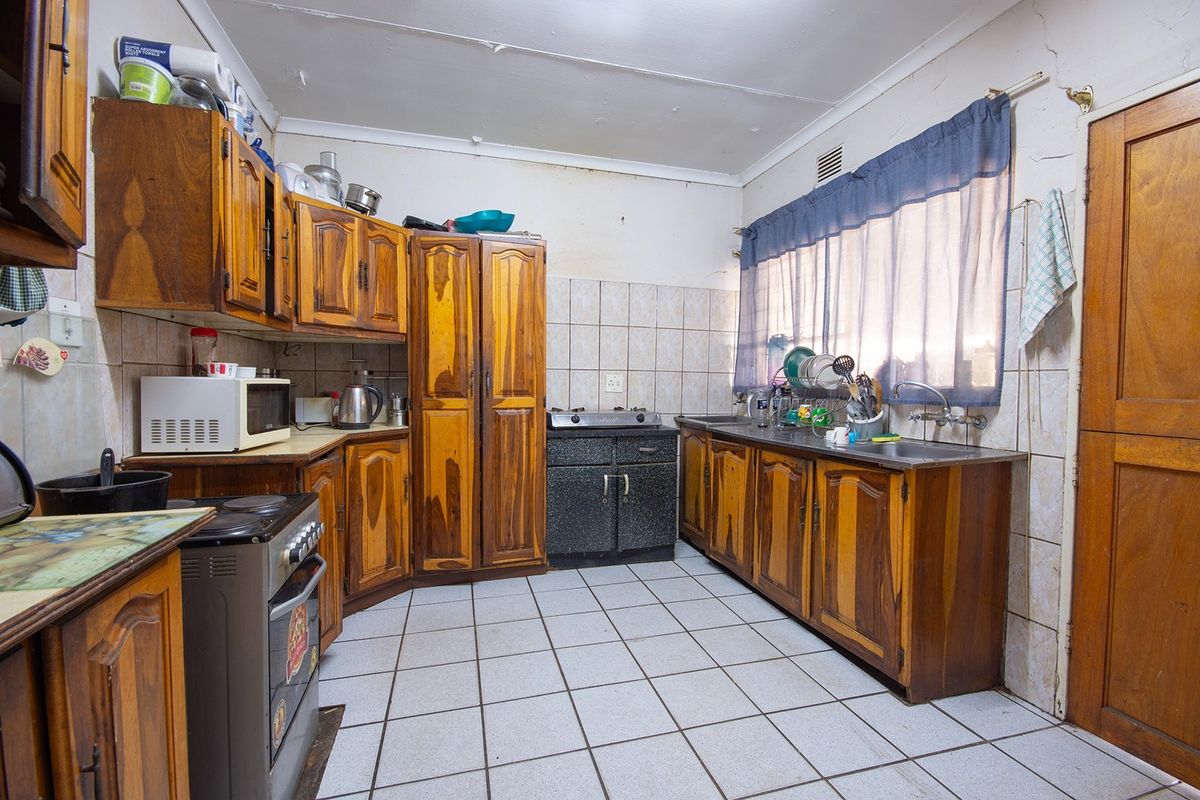 A dated kitchen featuring wooden cabinetry, tiled flooring, and a tiled backsplash, offering significant potential for modernization and renovation.