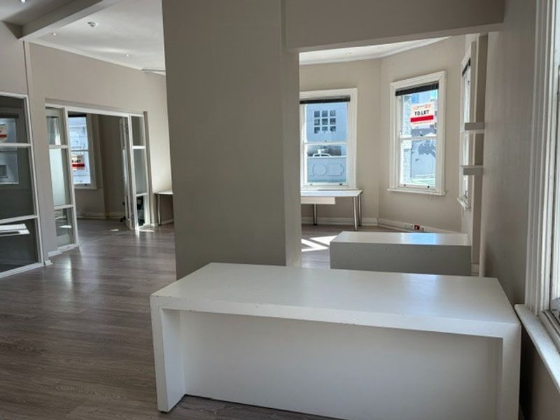 Spacious open-plan office area featuring modern laminate flooring, recessed lighting, and large sash windows providing ample natural light.