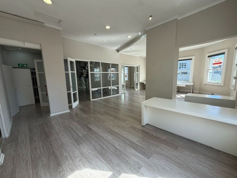 Spacious open-plan office area featuring modern laminate flooring, recessed lighting, glass partitions, and a built-in reception desk, offering a bright and professional workspace.