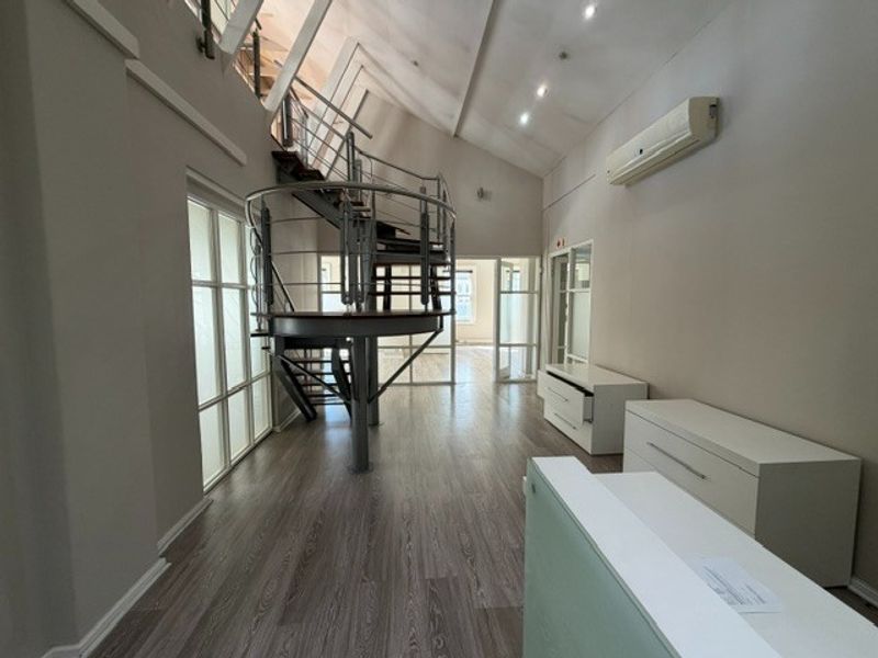 Spacious office area featuring a modern spiral staircase, high vaulted ceilings, recessed lighting, and durable laminate flooring with glass partition access.