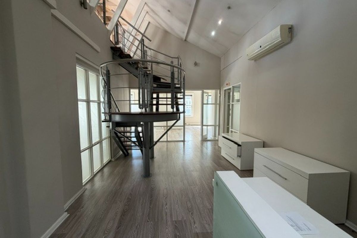 Spacious office area featuring a modern spiral staircase, high vaulted ceilings, recessed lighting, and durable laminate flooring with glass partition access.
