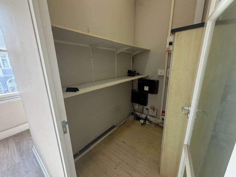 A small utility or storage space featuring wall-mounted shelving, timber flooring, and an exposed electrical distribution board.