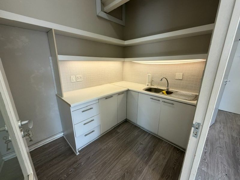 A clean and functional scullery or kitchenette area featuring white built-in cabinetry, a stainless steel sink, tiled backsplash, and modern floating shelving.
