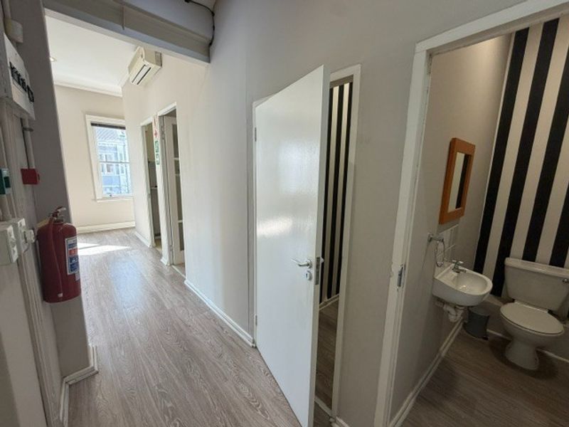 A functional office hallway featuring laminate flooring, a wall-mounted basin, and access to a private restroom facility.