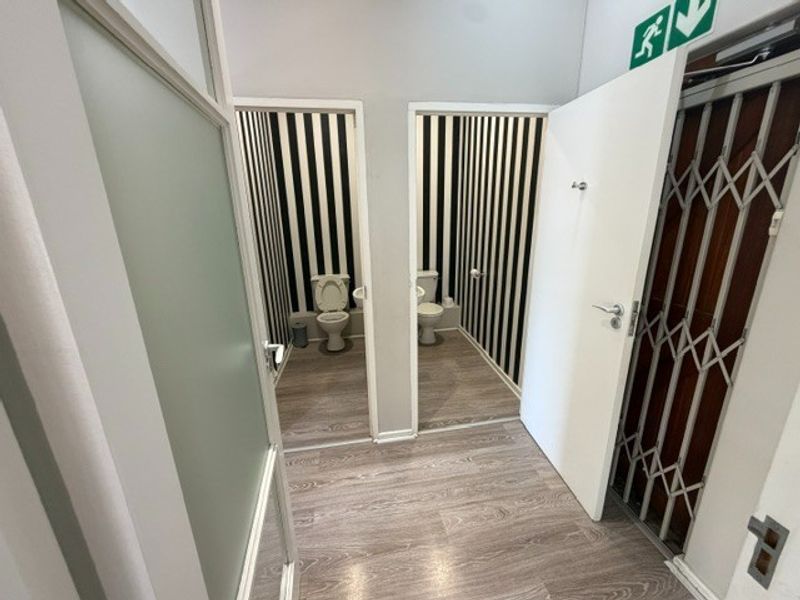 A clean office bathroom facility featuring two separate toilet cubicles with striped wallpaper and modern laminate flooring.