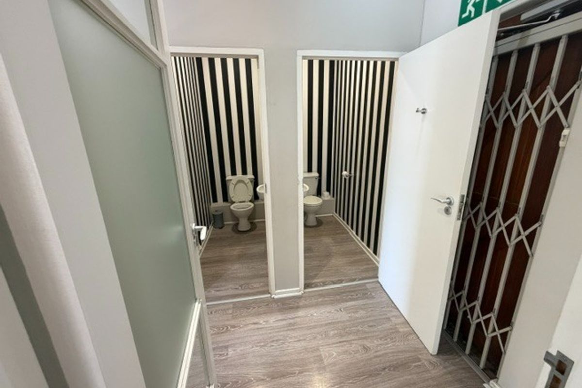 A clean office bathroom facility featuring two separate toilet cubicles with striped wallpaper and modern laminate flooring.
