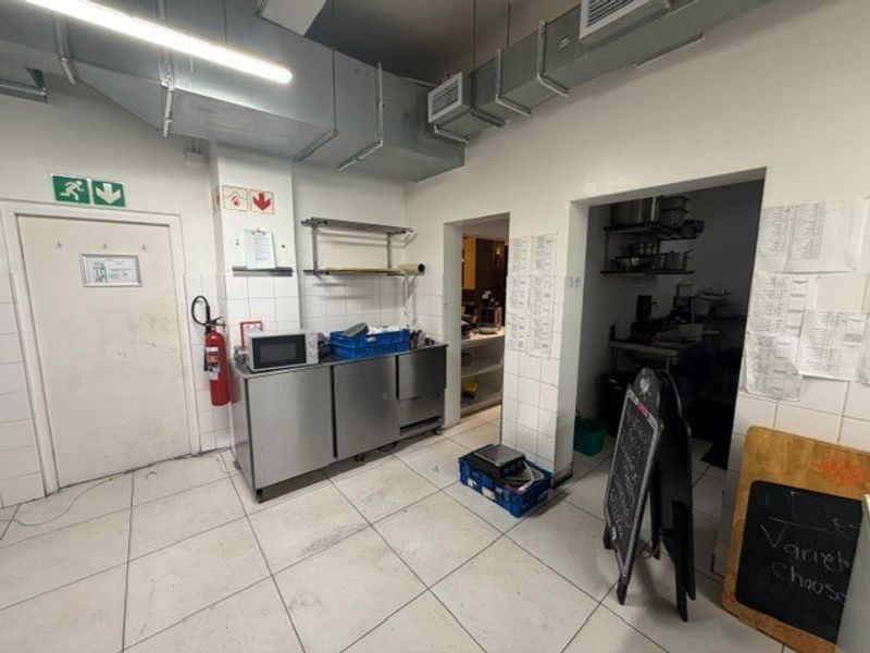 Commercial kitchen area featuring stainless steel prep counters, exposed ventilation ducting, and tiled finishes, providing a functional workspace for restaurant operations.