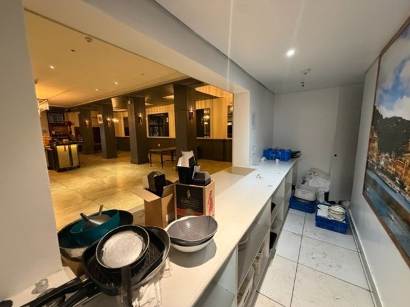A functional service and prep area featuring a long built-in counter, tiled flooring, and recessed lighting, connecting directly to the main restaurant dining space.