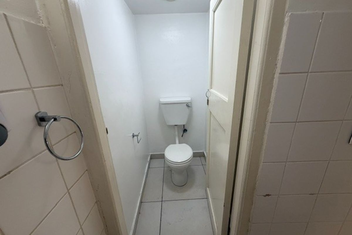 A small, functional restroom featuring a standard toilet, tiled walls, and tiled flooring, currently in need of cosmetic updates.