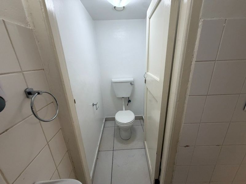 A small, functional restroom featuring a standard toilet, tiled walls, and tiled flooring, currently in need of cosmetic updates.