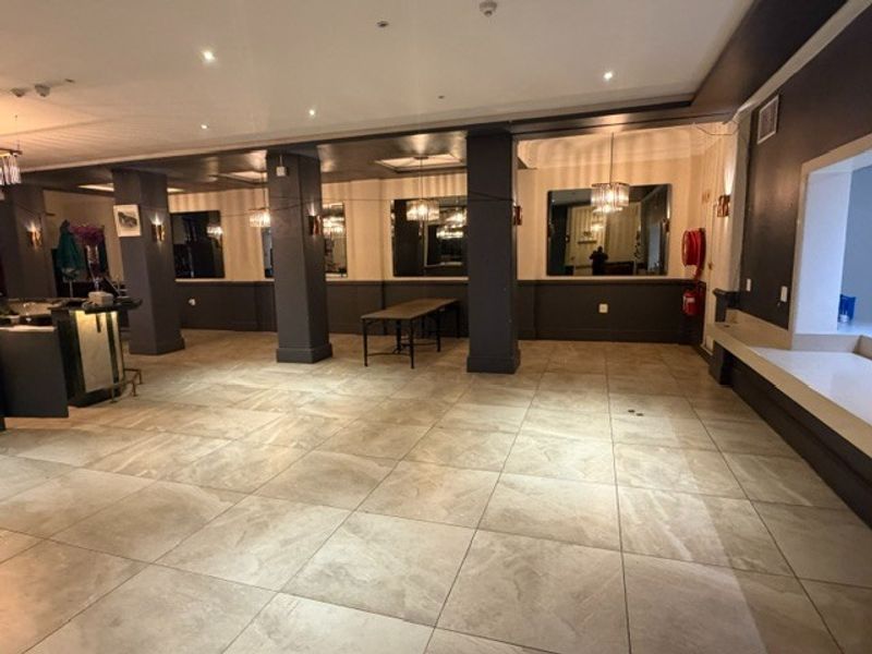 Spacious open-plan restaurant interior featuring large format floor tiles, structural columns, recessed lighting, and built-in service counters, offering a versatile layout for dining.