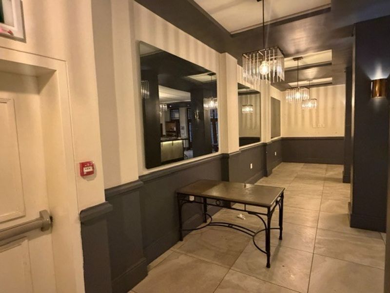 A well-maintained dining area featuring tiled flooring, decorative wainscoting, large wall-mounted mirrors, and elegant pendant lighting fixtures.