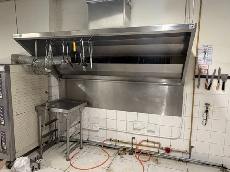 Commercial kitchen area featuring a large stainless steel extractor hood, tiled splashbacks, and integrated gas supply lines for professional cooking equipment.