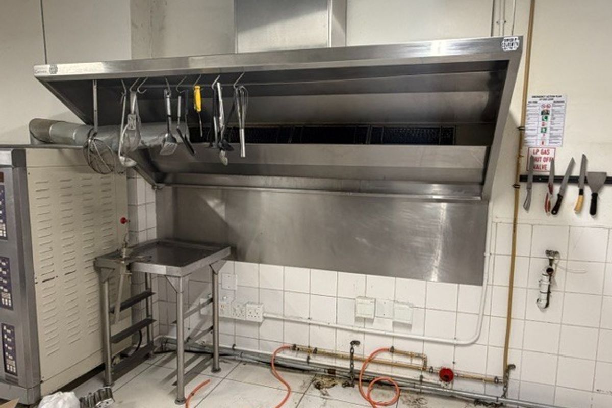 Commercial kitchen area featuring a large stainless steel extractor hood, tiled splashbacks, and integrated gas supply lines for professional cooking equipment.