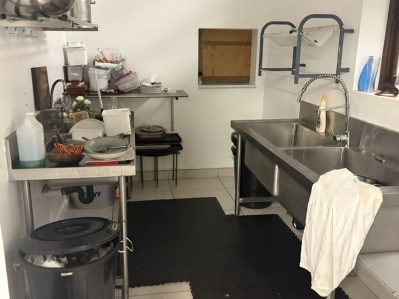A functional commercial scullery area featuring stainless steel double sinks, prep tables, and wall-mounted shelving, suitable for high-volume restaurant operations.