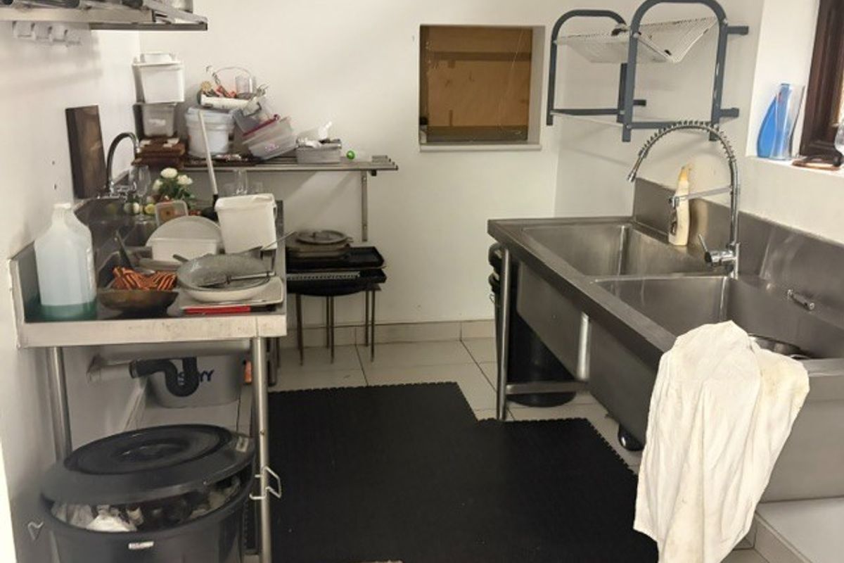A functional commercial scullery area featuring stainless steel double sinks, prep tables, and wall-mounted shelving, suitable for high-volume restaurant operations.